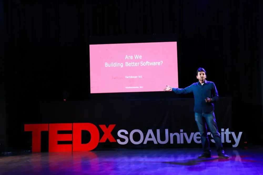 Karthikeyan NG on stage at TEDx SOA University, presenting a talk titled "Are We Building Better Software?"